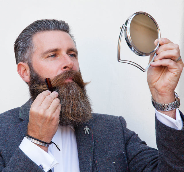 A man looking in the mirror combing his beard